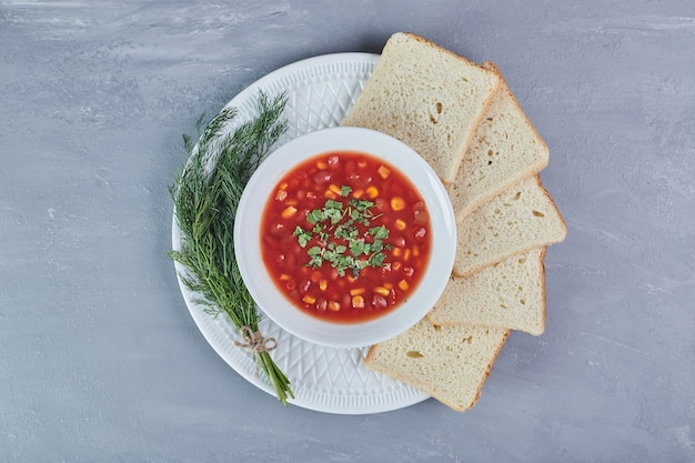 Maissuppe in Tomatensauce in einem weißen Teller mit Kräutern.