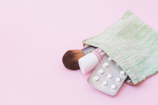 Make-up Pinsel; Nagellackflasche und weiße Pillenblisterpackung im Baumwollbeutel über rosa Hintergrund