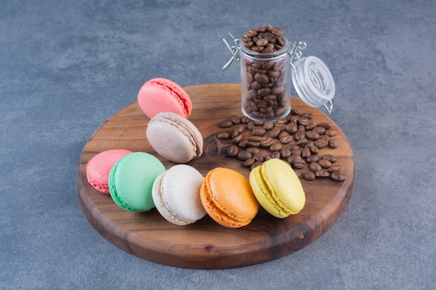 Makkaroni-Kekse in verschiedenen Farben mit Kaffeebohnen auf einem Holzbrett.