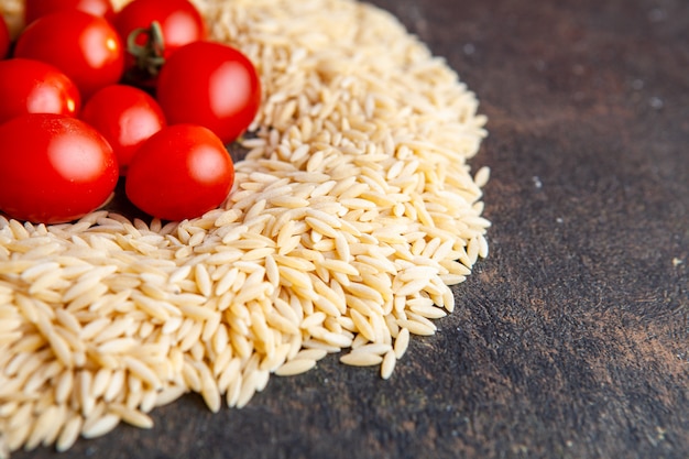 Makkaroni mit hoher Winkelansicht mit Tomaten auf ihnen auf dunklem strukturiertem Hintergrund. horizontal