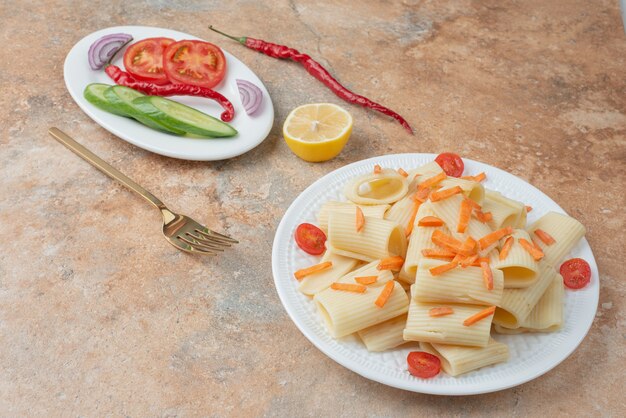 Makkaroni mit Karotte, Tomatenkirsche, Gurke und Zitronenscheibe auf weißem Teller