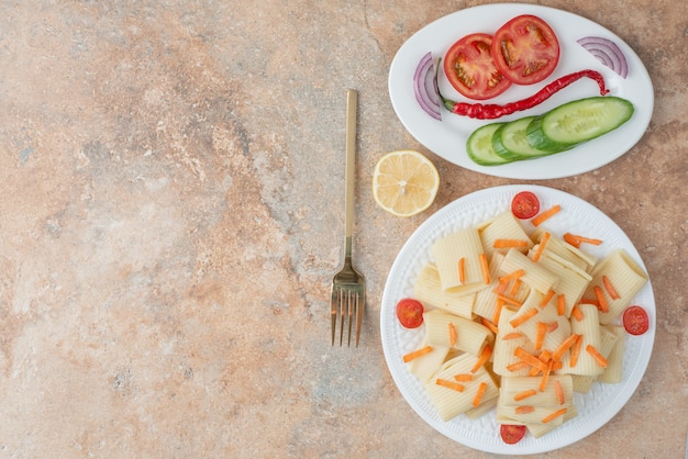 Makkaroni mit Karotte, Tomatenkirsche, Gurke und Zitronenscheibe auf weißem Teller