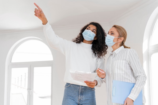 Maklerin mit medizinischer Maske, die Haus zur Frau zeigt