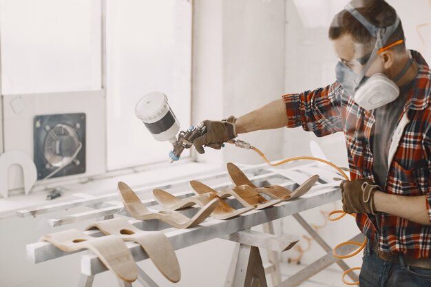 Malermeister in einer Fabrik, die Holz mit Spritzpistole malt