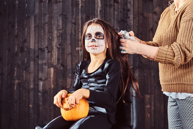 Mama macht Haarstyling mit einem Haarspray für die Halloween-Party. Halloween-Konzept.