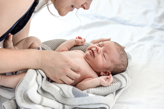 Mama spricht und lacht mit ihrem neugeborenen Sohn im Schlafzimmer zu Hause.