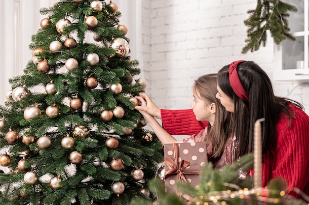 Mama und kleine Tochter schmücken gemeinsam den Weihnachtsbaum