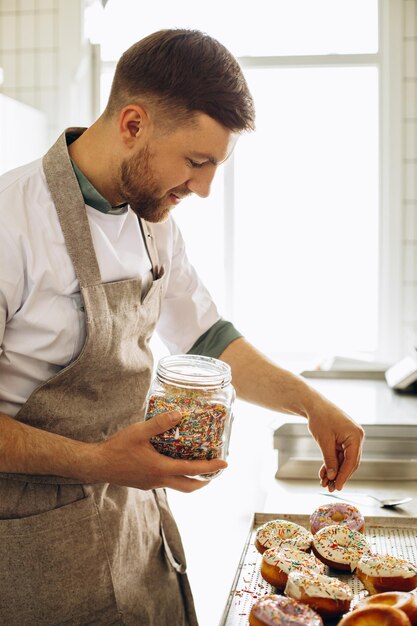 Kostenloses Foto man baker bestreut donuts mit bunten süßigkeiten