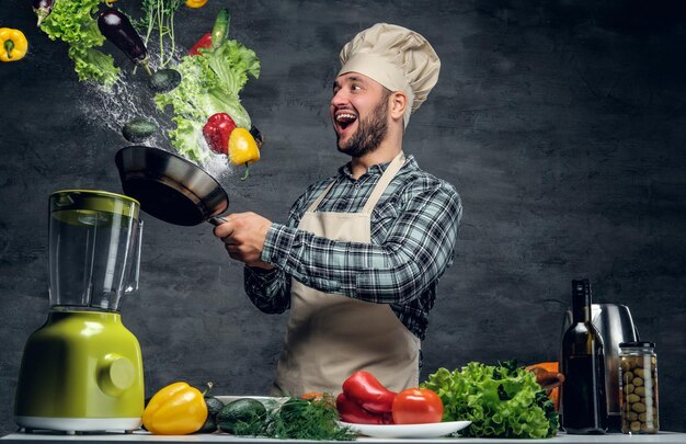 Man Cook hält eine Pfanne mit Gemüse in der Luft.