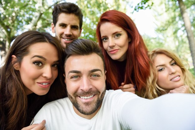 Man lächelt ein Selbst Foto von ihm zu nehmen und seine Freunde mit Bäumen im Hintergrund