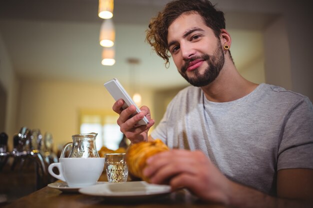 Man mit Handy während Croissant mit in CafÃ ©