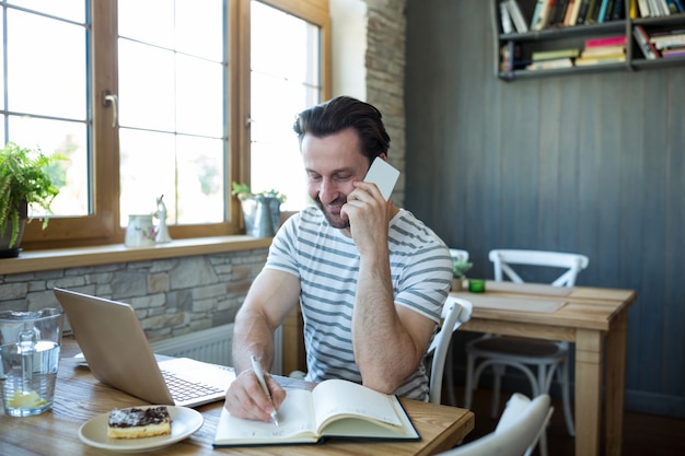 Man spricht über das Mobiltelefon und das Schreiben im Tagebuch im Coffee-Shop