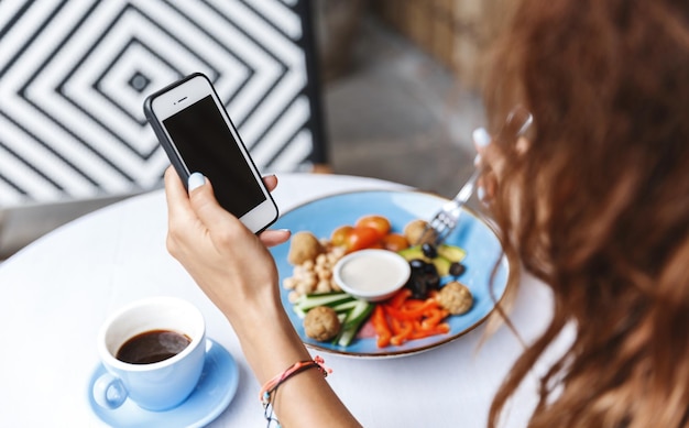 Management Diningout und People-Konzept Seitliche Schulteransicht der Hand der Frau mit dem Handy, das Nachrichten überprüft, während sie im Restaurant oder Café isst, kontaktieren Sie den Kunden während des Mittagessens