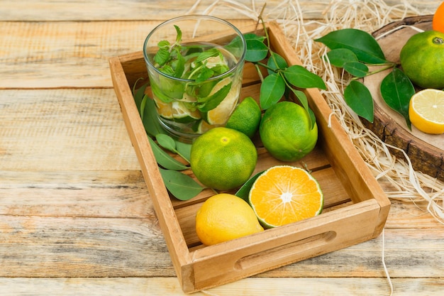 Mandarinen, Blätter und Entgiftungswasser in einer Holzkiste mit Mandarinen auf Holztisch