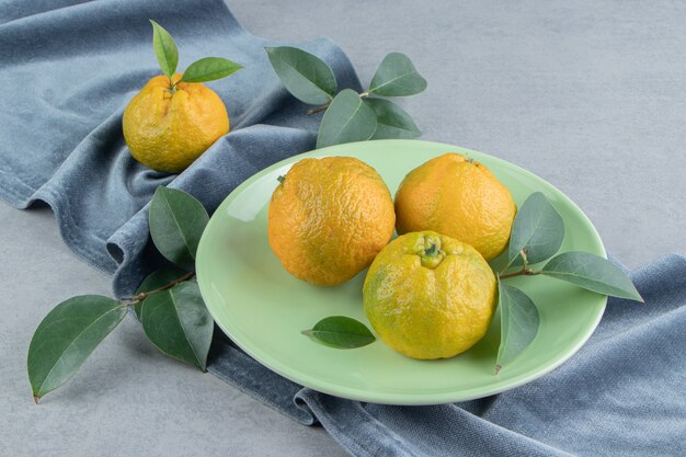 Mandarinen und Blätter auf einem Stück Stoff auf Marmor.