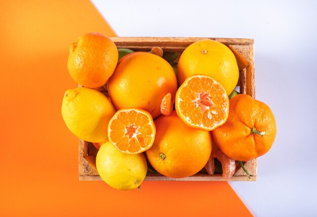 Mandarinenfrucht der orange Zitrusfrüchte in der Holzkiste auf gemischter orange und weißer Oberfläche