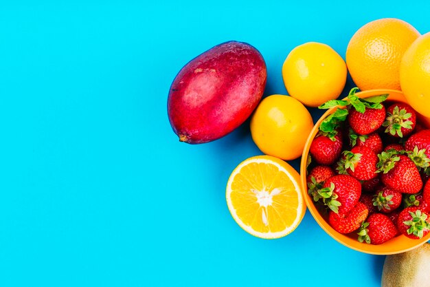 Mango; Orangen und Schüssel Erdbeeren auf blauem Hintergrund