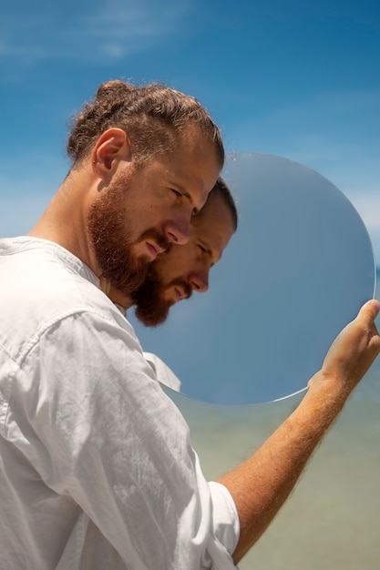 Mann am Strand posiert mit rundem reflektierendem Spiegel