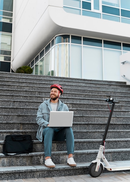 Kostenloses Foto mann arbeitet an seinem laptop neben seinem roller