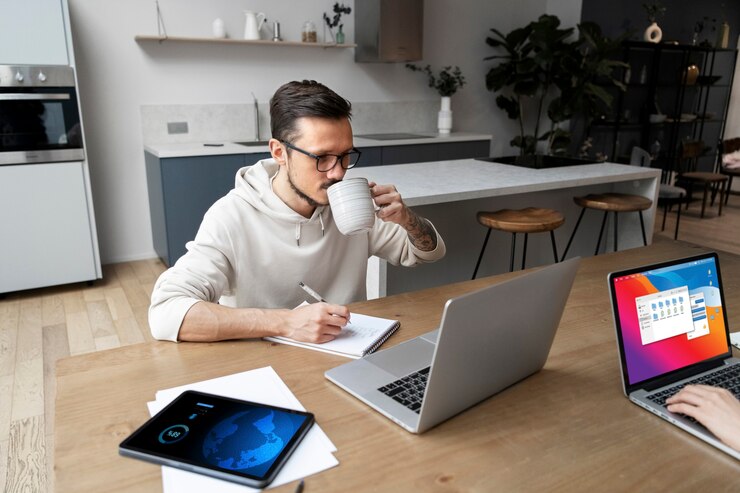 Kostenlose Foto mann arbeitet von zu hause an einem schreibtisch, während er etwas trinkt