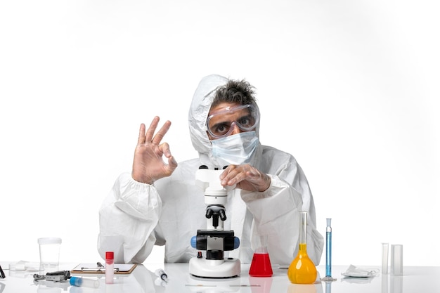 Mann Arzt in Schutzanzug und Maske mit seinem Mikroskop auf Weiß