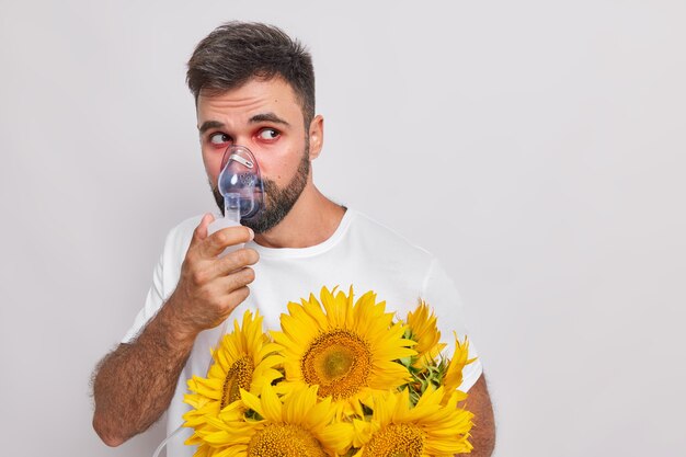 Mann atmet durch Sauerstoffmaske hat Allergie gegen Sonnenblumen rote tränende Augen schaut weg leidet unter Heuschnupfen Posen auf Weiß