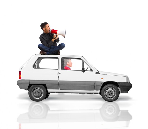 Mann auf dem Dach eines Autos sitzen für ein Megaphon schreien, während ein älterer Mann Laufwerke