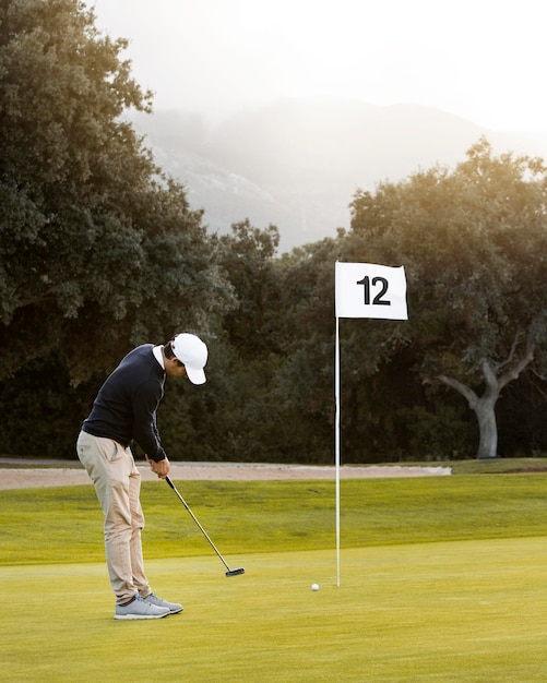 Mann auf dem Golfplatz, der neben Flagge spielt