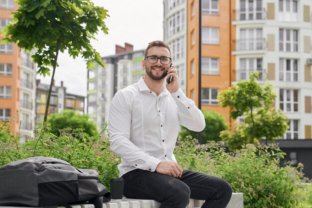 Mann auf der Bank, der per Telefon spricht und lächelnd in die Kamera schaut