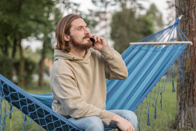 Mann auf Hängematte in der Natur, die auf Smartphone spricht