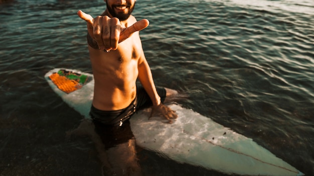 Mann auf Surfbrett im Meer, das Shaka-Handzeichen zeigt