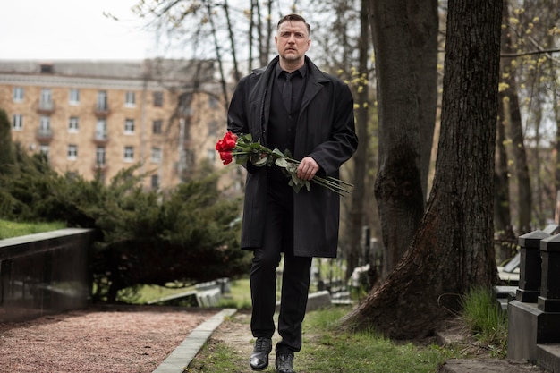 Kostenloses Foto mann bringt rosen zu einem grabstein auf dem friedhof