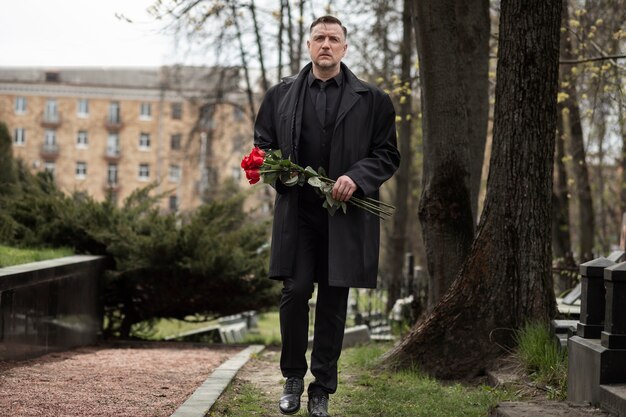 Mann bringt Rosen zu einem Grabstein auf dem Friedhof