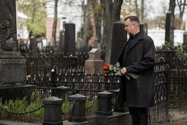 Kostenloses Foto mann bringt rosen zu einem grabstein auf dem friedhof