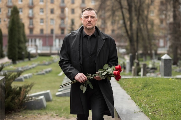 Mann bringt Rosen zu einem Grabstein auf dem Friedhof