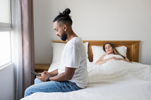 Mann checkt sein Handy im Bett neben seiner Frau