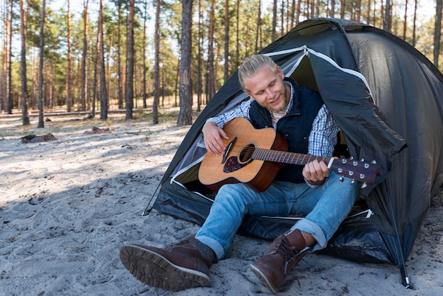 Mann, der akustische Gitarre spielt und in seinem Zelt sitzt