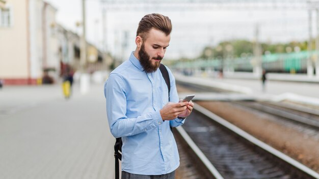 Mann, der am Bahnhof unter Verwendung des Handys steht