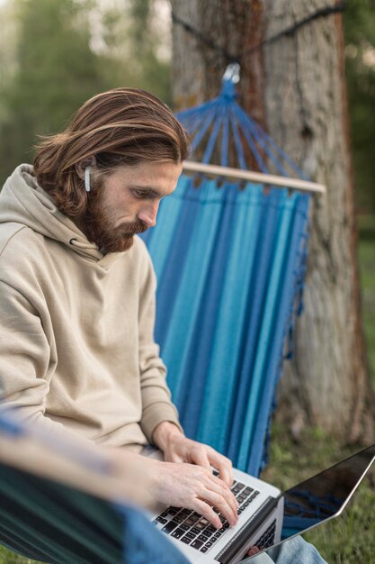 Mann, der am Laptop arbeitet, während er in der Hängematte sitzt