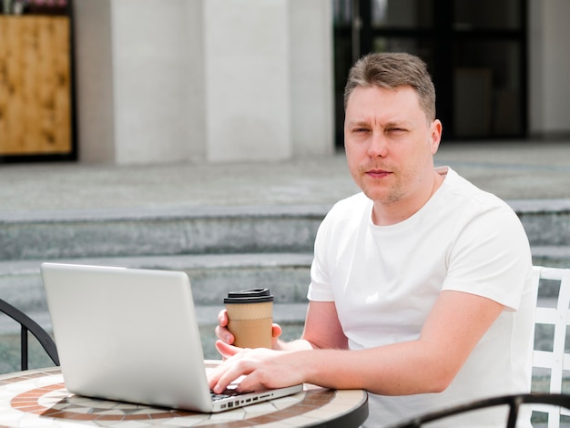 Mann, der am Laptop im Freien beim Kaffee arbeitet