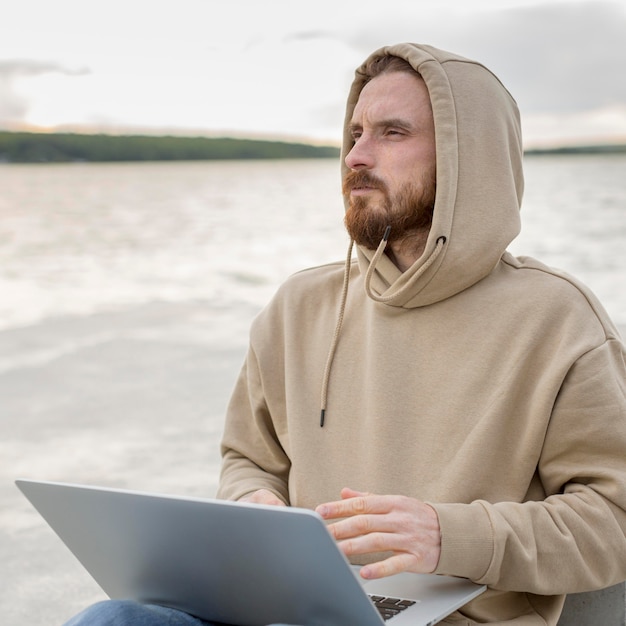 Mann, der am Laptop neben See arbeitet