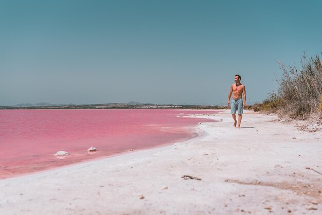 Mann, der am Strand in der Nähe des rosafarbenen Meeres spazieren geht