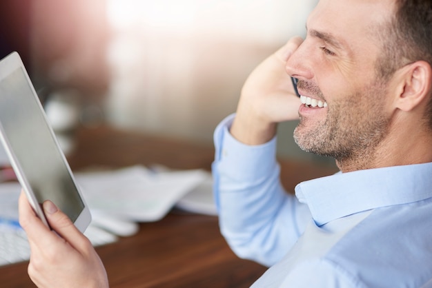 Mann, der am Telefon spricht und digitales Tablett durchsucht