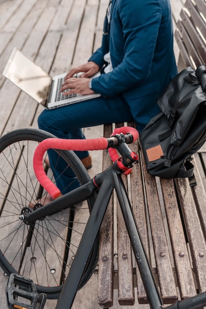 Kostenloses Foto mann, der an laptop neben seinem fahrrad draußen arbeitet