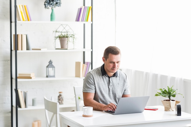 Mann, der an Laptop über Schreibtisch arbeitet