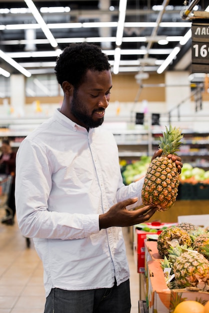 Kostenloses Foto mann, der ananas im gemischtwarenladen kontrolliert