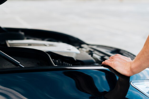 Mann, der auf Auto mit offener Haube sich lehnt