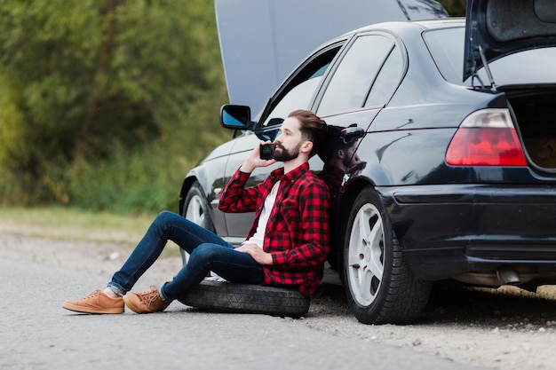 Mann, der auf Auto sich lehnt und am Telefon spricht