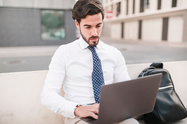 Mann, der auf Bank unter Verwendung des Laptops sitzt