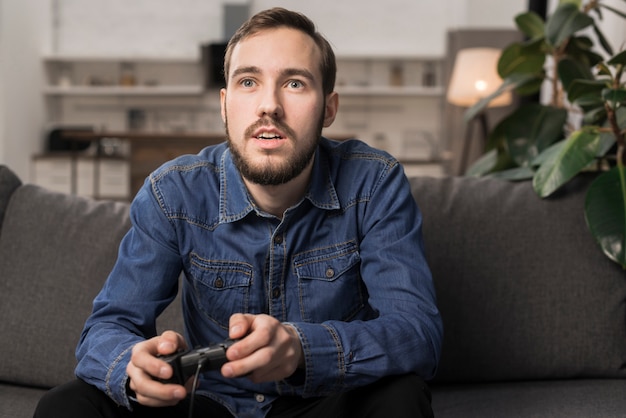 Mann, der auf Couch sitzt und Gamecontroller hält